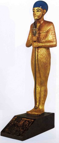 Ptah con un casquete, collar menat, cetro uas con el pilar Dyed y el Anj. Es de resaltar el extremo parecido de la estatuilla del Oscar con esta de Ptah.
